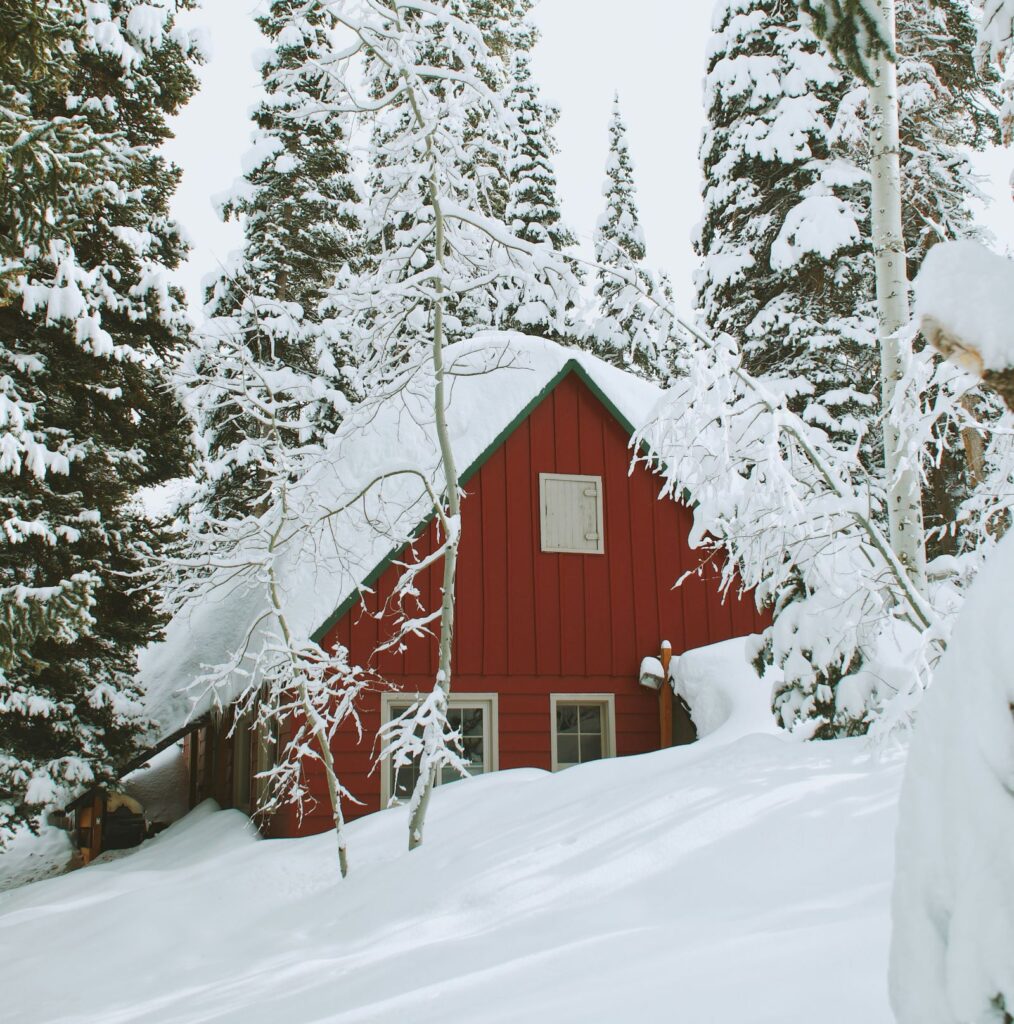 A red house buried in snow up to the bottom of the window.s