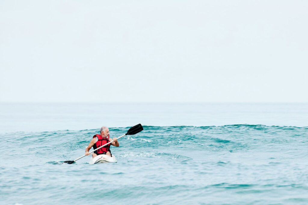 a man kayaks in an ocean with some swells behind him