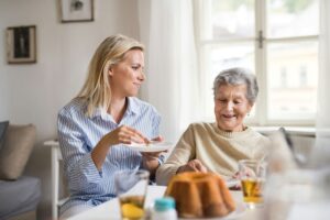 Two women in a retirement home in front of a window, drinking iced tea and eating pound cake. One is the adult daughter of the other woman.